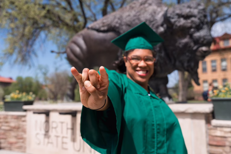 NDSU Transition and Access Program graduate Alexander Aikens posing in front of the Bison Statue at NDSU.